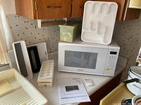 Wide angle photo of Panasonic microwave, manual, and various plastic cutlery organizers, ice cube trays on kitchen counter.