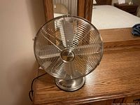 Front view of the Uberhaus retro look table fan in chrome finish showing the metal blade guard and three blades.