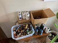 Photo showing a plastic bin filled with assorted small spools of thread in various colors and large cones of thread beside it on a table.