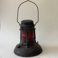 Front view of railroad lantern with metal handle up, black metal base and housing, red glass globe embossed Dietz No. 40.