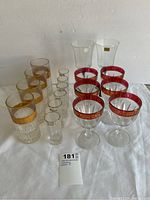 Full lot overview showing 4 highball tumblers with gold band, 6 cranberry cordial glasses with gold rims, 2 clear Luminarc Octime glasses, and 6 small shot glasses