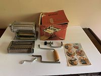 Grazia pasta maker with two rollers, wooden and metal crank handles, and metal clamp displayed with original box