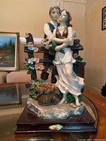 Full view of La Anina Collection statue showing couple with flowers and wooden fence on wooden base