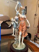 Full view of the La Anina Collection statue showing a woman and cherub on a wooden base in a room.