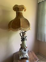 Full view of tall 1960s Italian figurine table lamp with fabric fringed lampshade on ornate base