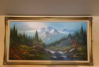 Full view of the framed oil painting showing mountain landscape with river and forest in gold decorative frame.