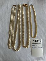 Four pearl necklaces laid flat showing length and clasps, including two freshwater pearl strands and two faux pearl strands.