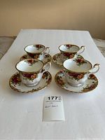 Four teacups on saucers, all decorated with roses and gold trim, arranged in a square