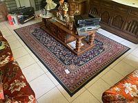 View of rectangular area rug on tiled floor with wooden coffee table and other furniture nearby.