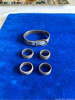 All jewelry items on blue velvet background: one adjustable sterling silver bracelet and four silver rings with various patterns.