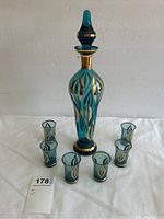 Decanter with stopper and six shot glasses arranged on white cloth, lot tag visible