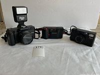 Front view of three vintage film cameras arranged side by side; includes a large Orion flash on the left camera