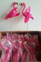 Two pink plastic flamingo yard ornaments with metal stakes and spinning wings, packed inside a box with bubble wrap