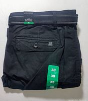 Folded black cargo shorts with buttoned flap pocket and green size 38 tags visible, showing Buffalo David Bitton brand label and belt with striped stitching detail.