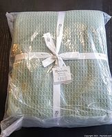 Packaged Rivancia woven waffle weave blanket in sage green tied with white branded ribbon.