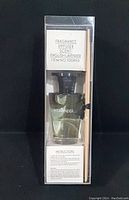 Fragrance diffuser bottle with liquid and diffuser sticks visible inside clear plastic packaging with product details and instructions on label.