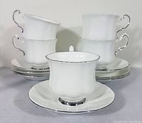 Set of five white demitasse cups stacked and arranged with five matching saucers. The cups have curved handles and platinum edge trim.