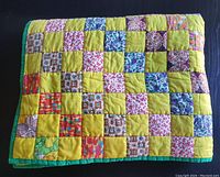 Folded vintage handcrafted patchwork quilt showing the alternating yellow and patterned squares and green border.
