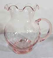 Left side view of the pink depression glass pitcher showing the swirl pattern and ruffled top edge with the solid pink handle and base.
