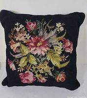 Front view of the embroidered floral cushion showing detailed needlework of flowers in various colors against black background.
