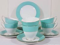 Photo showing full set of six footed teacups arranged on six saucers in front of six salad plates with turquoise and gold trim.