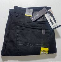 Folded pair of black denim pants with Buffalo David Bitton branding tags visible. Yellow size sticker 32x32 on back pocket.