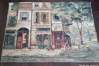 Full view of the large tapestry showing Paris shops and outdoor seating in a street scene.