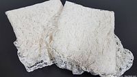 Photo of two off-white vintage lace curtain panels folded, showing attached valence with decorative scalloped lace edging.
