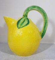 Side view of the lemon-shaped yellow ceramic pitcher with a curved green handle and leaf detail.