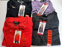 Four Buffalo David Bitton ladies' long sleeve knit tops in medium size, folded and displayed with tags, showing black, purple, red with hearts, and dark grey colors.