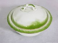 Front side view of semi-porcelain bowl lid showing green rim and ornate handle