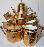 Full set arranged with all cups stacked on saucers, sugar bowl, creamer, and coffee pot prominently displayed. Visible ornate gilding and red jewel accents.
