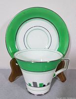 Teacup displayed in front of saucer, showing the front and side views of the green band with silver trim and geometric patterns.