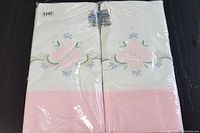 Photo of two pillowcases in original plastic packaging, showing pink band and stitched floral applique design.