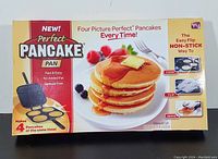 Front of box showing the product, Perfect Pancake Pan, with label highlighting features like fast & easy, no added fat, spatula free