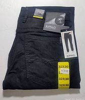 Folded black denim jeans showing back pocket and attached labels and tags with brand, size and model information.