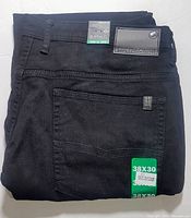 Front view of folded black denim jeans showing back pocket, leather brand patch on waistband, and size stickers.