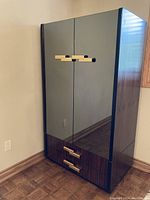 Closed armoire showing veneer finish with mirrored doors and three gold-tone handles.
