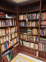 Wide view showing the wood bookcase fully stacked with books, corner shot showing the polished medium brown wood and shelving depth.