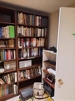 Full view of tall wood bookcase filled with books and some items on the floor nearby, showing overall size and shelving.