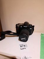 Front view of Nikon D70 DSLR camera with lens and attached strap on white surface.