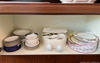 Shelved collection of mixed fine china: bowls, plates, cups, saucers, and two white Rosenthal salt and pepper shakers in front.