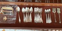 Full view of the assorted flatware laid out with spoons, forks, tongs, a brush and tray in a drawer