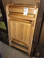 Image of six wooden folding chairs stacked upright showing the front and seat panels.