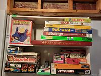 Photo showing stacked boxed games including Bingo, Stratego, 15 Love, Careers, Poleconomy, Superfection, Upwords, Probe, Simon indicated on box, and small scissors and chalk.