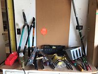 Photo showing various garden tools including long-handled hedge shears, hand tools, and a tool rack.