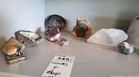 Full view of the assorted geodes and mineral stones arranged on a shelf including quartz, amethyst, and green crystal stones, along with a mining trophy.