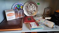 Group photo showing a boxed set of Manischewitz Shabbat candles, two decorative plates, multiple religious books, a scroll, and some folded fabric (likely Kippot).