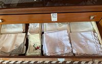 Drawer showing various folded linen napkins and placemats with embroidery and scalloped edges.