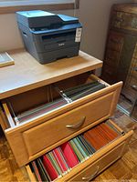 Brother printer on top of wooden cabinet with two open drawers showing hanging file folders